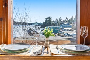 A table set for two with a vase of flowers, a wine glass, and a view of a waterfront.