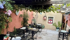 Un patio al aire libre con mesas y sillas, una pared rústica y plantas colgantes.