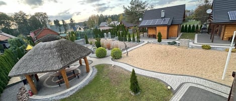 A residential area with a sandy courtyard, a wooden gazebo, and houses with solar panels.
