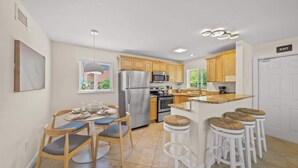 A modern kitchen with a central island, wooden cabinets, stainless steel appliances, and a dining area with chairs and a table. - Salty Summer – Steps to Siesta Key Village & Beach (Siesta Key)