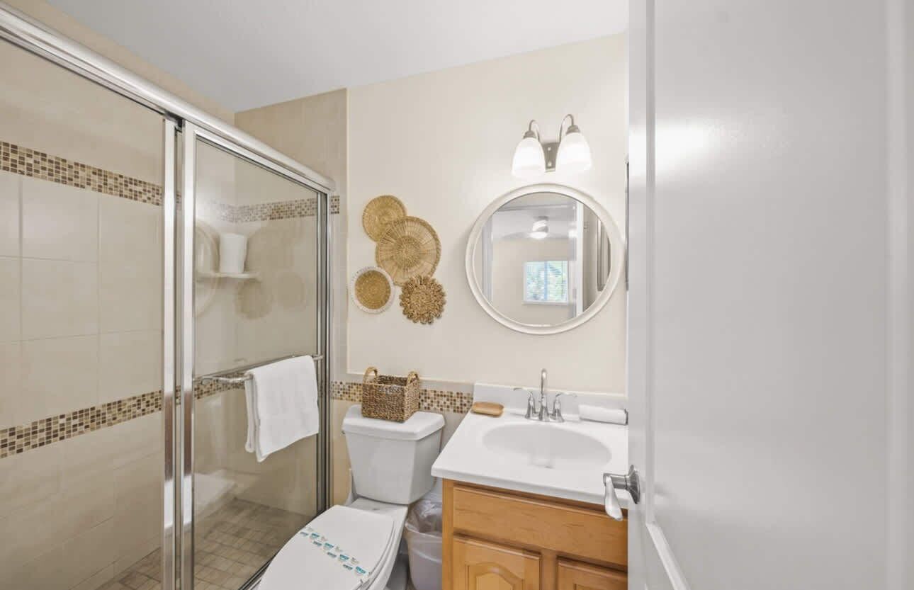 A bathroom with a glass shower enclosure, a toilet, a sink with a mirror above it, and decorative wall art.
