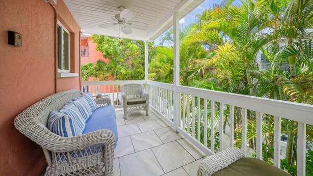 A covered balcony with wicker furniture, a ceiling fan, and lush tropical plants. - Salty Summer – Steps to Siesta Key Village & Beach (Siesta Key)