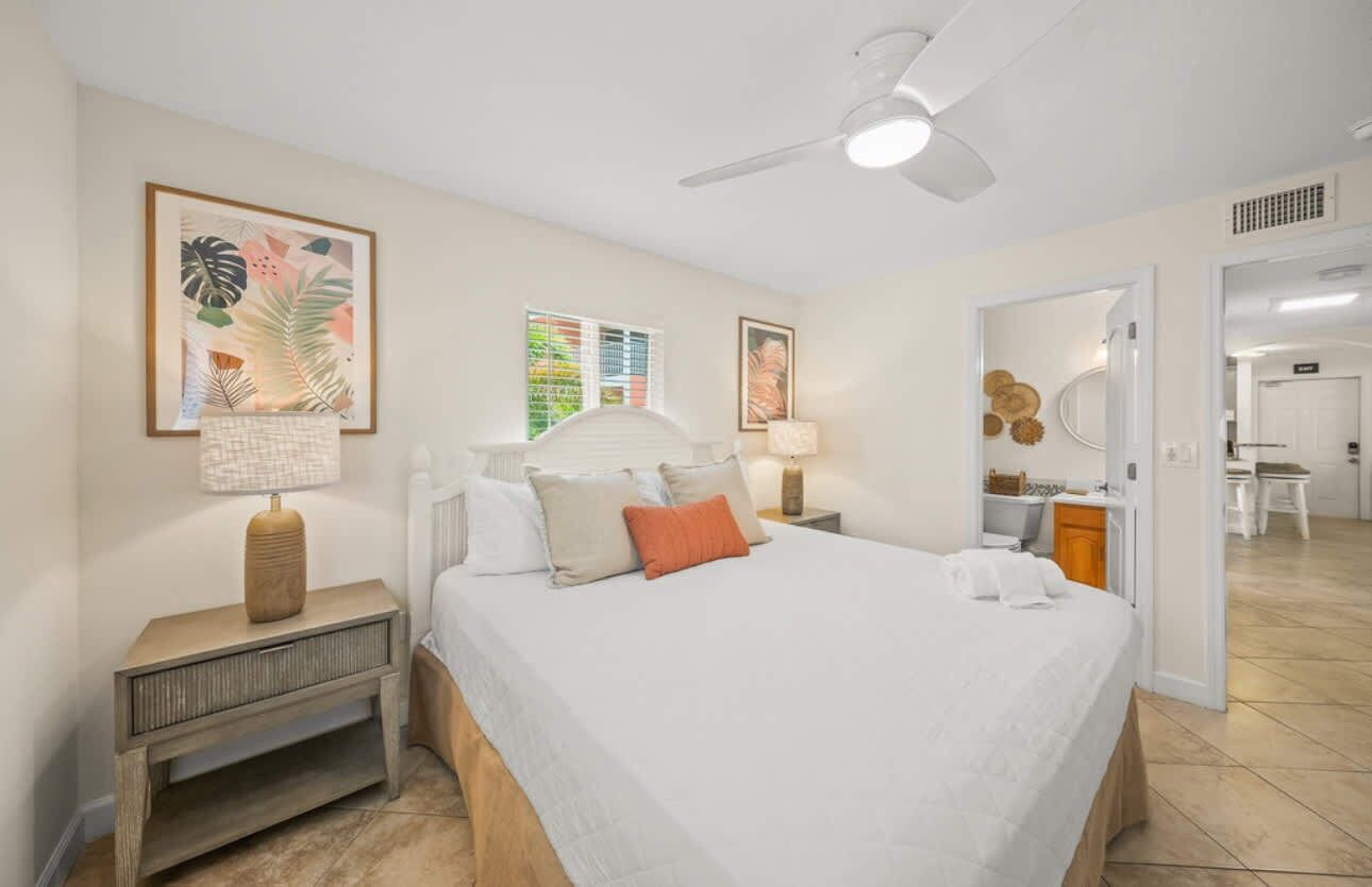 A bedroom with a bed, bedside tables, a ceiling fan, and artwork on the walls.