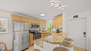 A modern kitchen with wooden cabinets, stainless steel appliances, a granite countertop island with stools, and an exit sign. - Salty Summer – Steps to Siesta Key Village & Beach (Siesta Key)