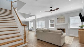 A spacious living room with a wooden staircase, a large sofa, and a ceiling fan. - The Pool House~Steps to Beach & Siesta Key Village (Siesta Key)