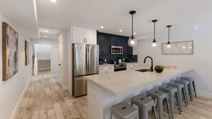 A modern kitchen with a central island, stainless steel appliances, and bar stools. - Island House – Walk to Siesta Key Beach! (Siesta Key)