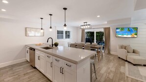 A modern kitchen with a central island, pendant lighting, and a dining area with a view of the outdoors. - Island House – Walk to Siesta Key Beach! (Siesta Key)