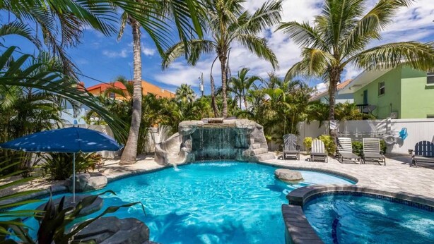 A swimming pool with a waterfall feature, surrounded by palm trees and lounge chairs. - Island House – Walk to Siesta Key Beach! (Siesta Key)
