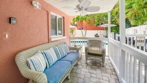 A covered outdoor seating area with a wicker sofa and chairs, a ceiling fan, and a view of the pool and greenery. - Summer Salt – Steps to Siesta Key Village & Beach (Siesta Key)