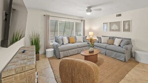 A living room with a grey sofa, a wooden coffee table, a TV mounted on the wall, and a ceiling fan. - Summer Salt – Steps to Siesta Key Village & Beach (Siesta Key)