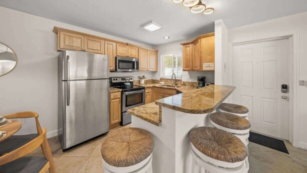 A modern kitchen with stainless steel appliances, wooden cabinets, and a granite countertop. - Summer Salt – Steps to Siesta Key Village & Beach (Siesta Key)
