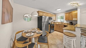 A modern kitchen with wooden cabinets, stainless steel appliances, and a dining area with a round table and bar stools. - Summer Salt – Steps to Siesta Key Village & Beach (Siesta Key)