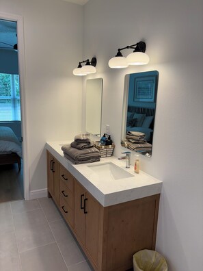 Een badkamer met een witte wastafel, houten kastjes, een grote spiegel en twee wandlampen.