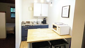 Una cocina compacta con una mesa de madera y taburetes, estufa, microondas y lámparas colgantes.