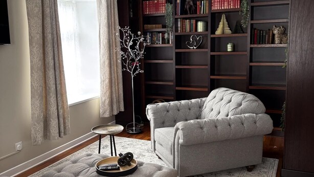 A living room with a grey sofa, a matching ottoman, and a bookshelf filled with books and decorative items. - Corraleith/Cozy 2 Bedroom/2 Bath Leith Flat: Tram at Ocean Terminal: Parking (Edinburgh)