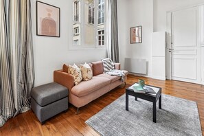 Un salon moderne avec un canapé, un pouf et une table basse, une fenêtre avec des rideaux et une porte.