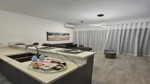 Ein modernes Hotelzimmer mit Küchenzeile, einem Esstisch und einem großen Fenster mit Vorhängen.