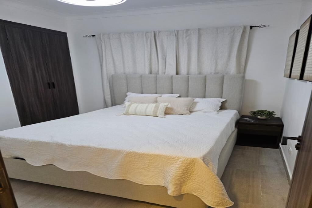 A bedroom with a large bed, a nightstand with a plant, and a dark wooden wardrobe.