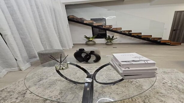 Ein modernes Wohnzimmer mit einem Glastisch, einer Couch und einer Treppe, die in ein Obergeschoss führt.