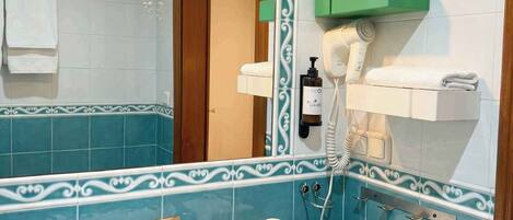 Un baño con un lavabo blanco, un espejo con marco decorativo, un perchero y un estante verde con un secador de pelo.