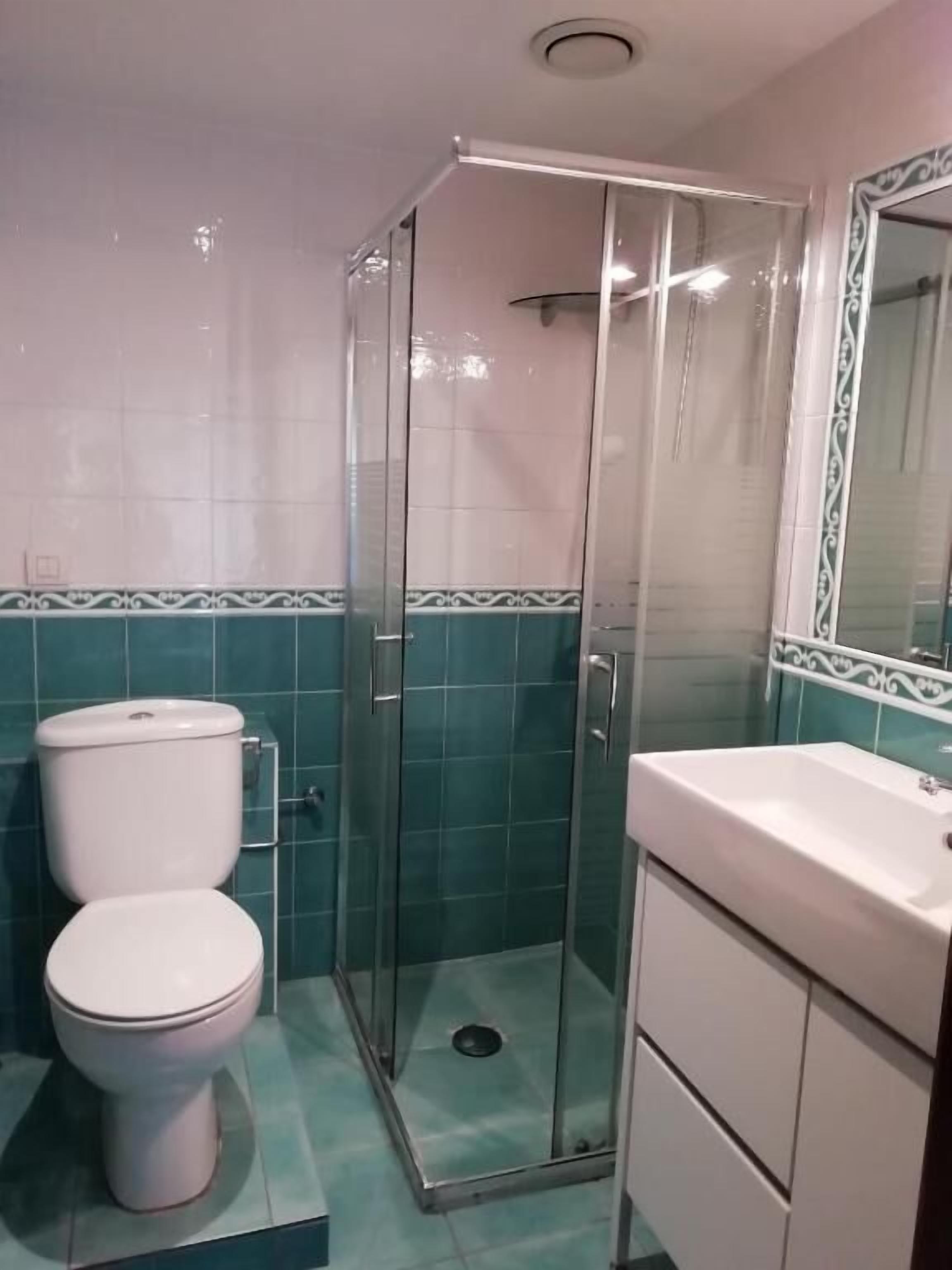 A bathroom with a toilet, a glass-enclosed shower, and a vanity with a mirror.