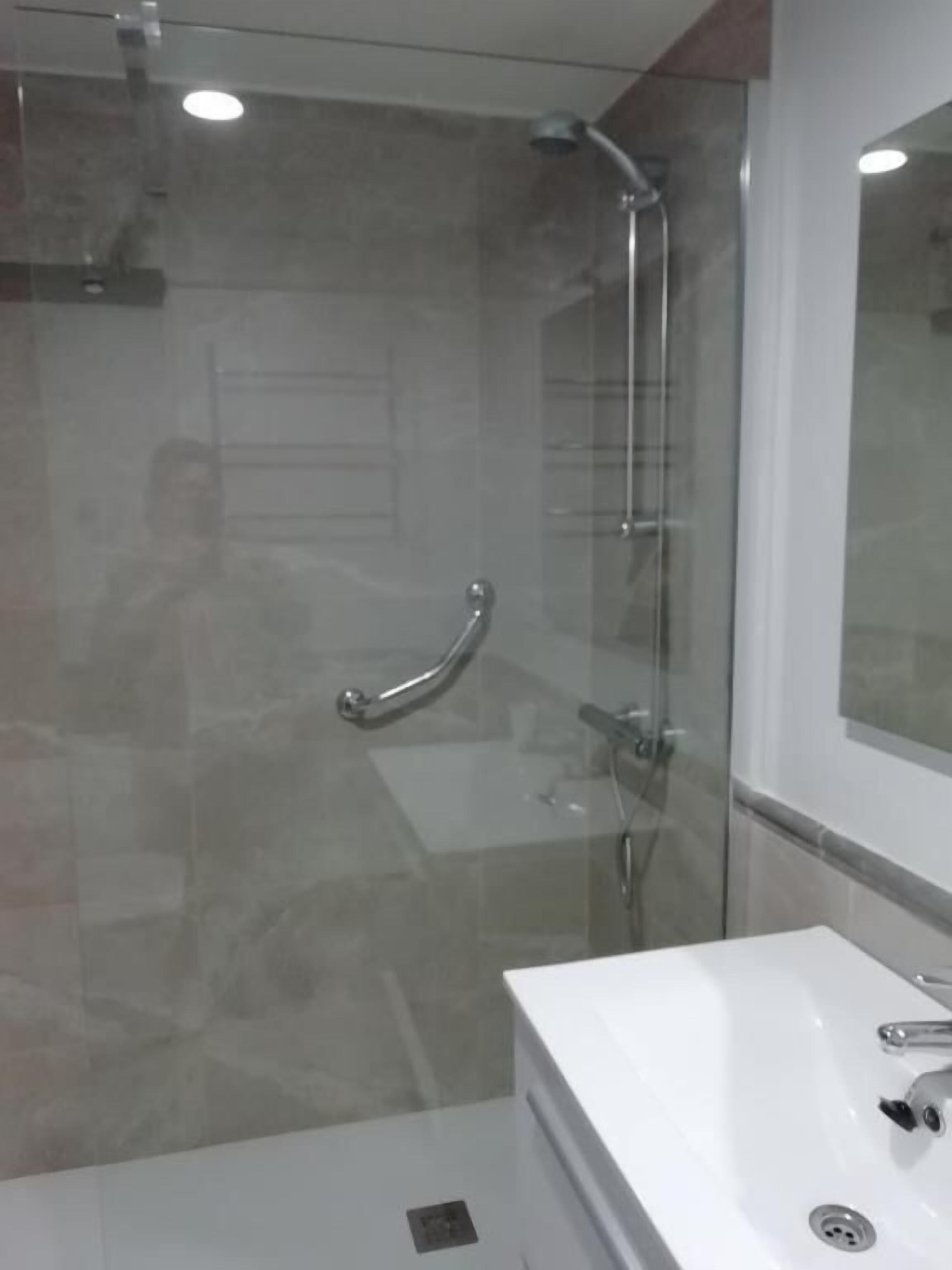 A modern bathroom with a glass-enclosed shower, a white sink, and a large mirror.