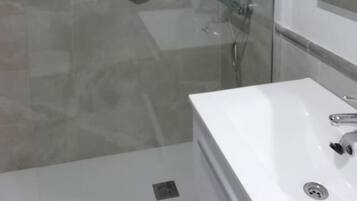 A modern bathroom with a glass-enclosed shower, a white sink, and a large mirror.