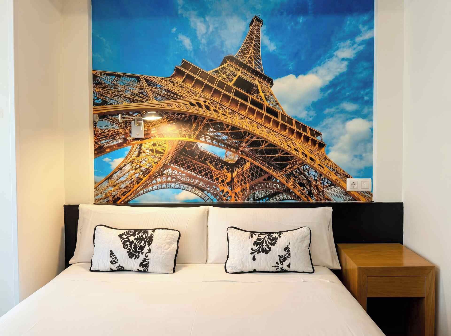 A bed with two pillows, a nightstand, and a large poster of the Eiffel Tower.