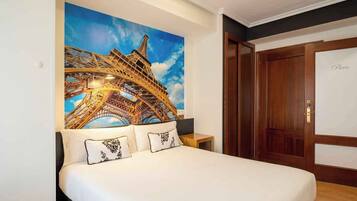 Un dormitorio con un gran mural en la pared de la Torre Eiffel, una puerta de madera y una cama con ropa de cama blanca.
