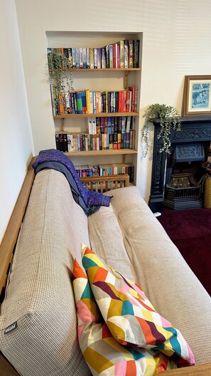 A cozy room with a sofa, a bookshelf filled with books, and a fireplace. - 4 Bed Private Victorian Town House - Central Headington - Oxford (Oxford)