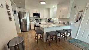 A modern kitchen with stainless steel appliances, a marble countertop, and wooden stools. - Cozy Little Slice of OCMD Heaven (Ocean City)
