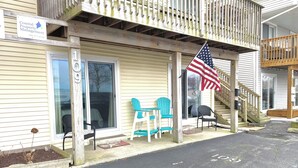 A coastal property management office with a wooden porch, two chairs, an American flag, and a staircase leading to an upper level. - Cozy Little Slice of OCMD Heaven (Ocean City)