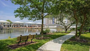 A waterfront park with a bench, a walking path, and a row of buildings with a water body in the background. - Cozy Little Slice of OCMD Heaven (Ocean City)