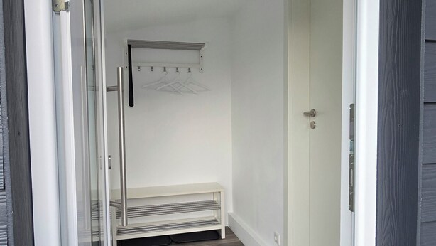 A narrow hallway with a bench, a coat rack, and a door leading to a room.
