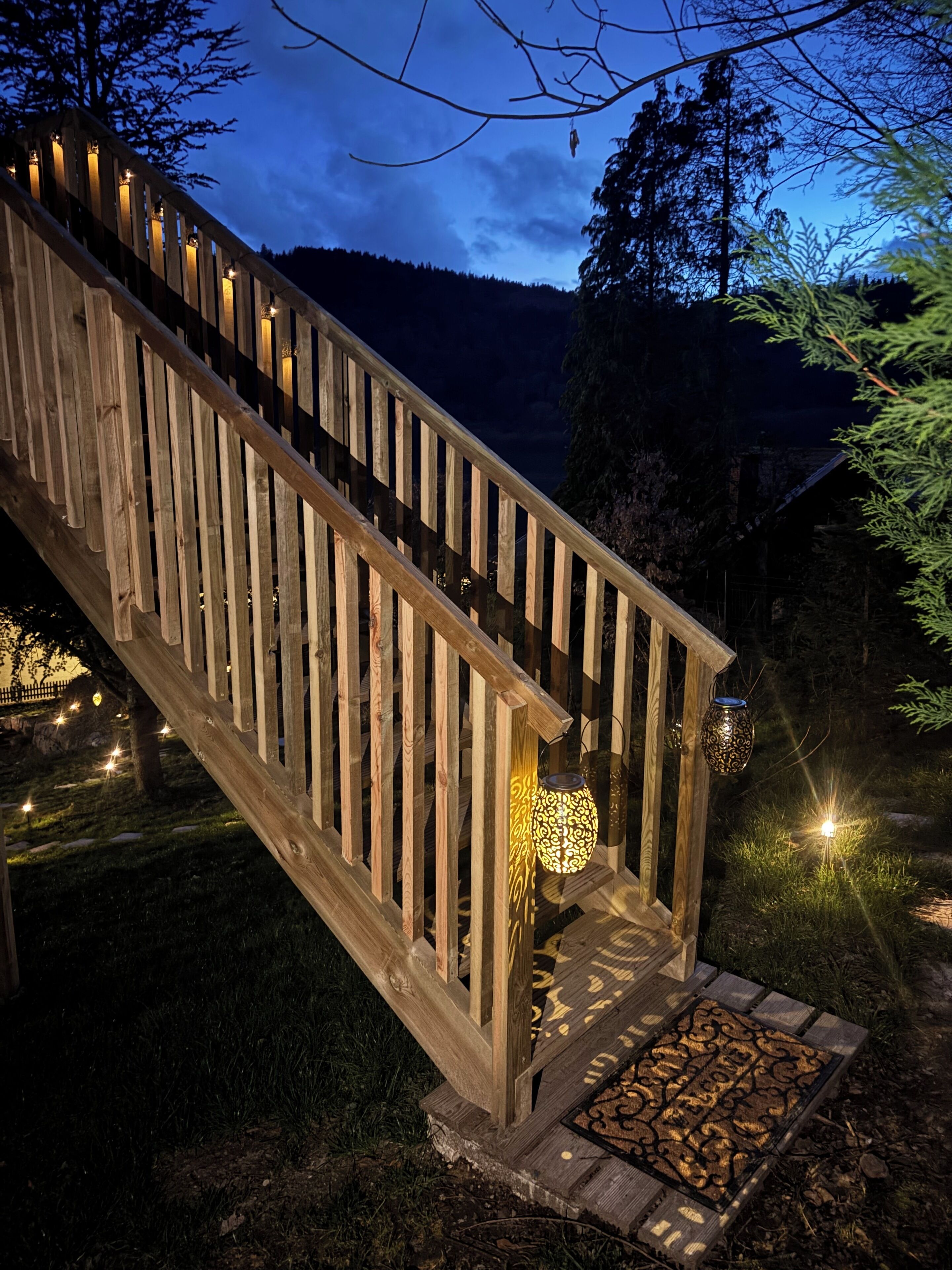 A wooden staircase with a railing, leading to a porch area with decorative lighting.