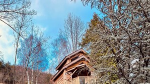 Una baita di legno con una scala che conduce a un balcone, circondata da alberi e erba.