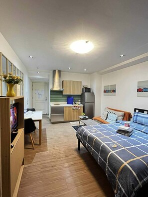 A compact hotel room with a kitchenette, a bed with a blue and white patterned bedspread, a small dining table, and a TV. - Stay in Makati’s amenity-rich luxury condo (Makati)