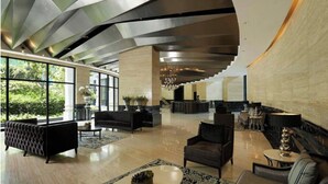 Un hall amplio con diseño moderno, que incluye un mostrador de recepción, zonas de estar y grandes ventanales con vistas al exterior.