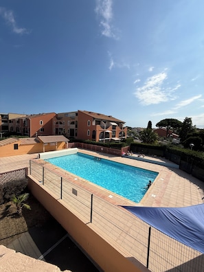 A swimming pool surrounded by a fenced area with a building in the background.