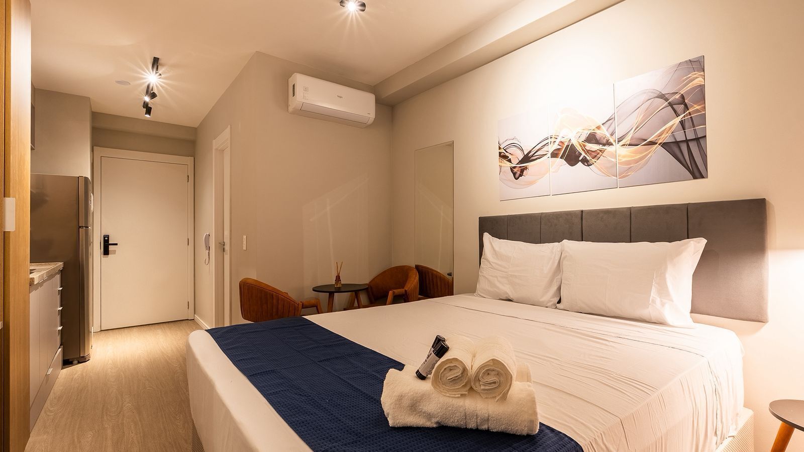 Una camera d'albergo con un letto, una scrivania, una sedia, un condizionatore d'aria e un quadro appeso al muro.