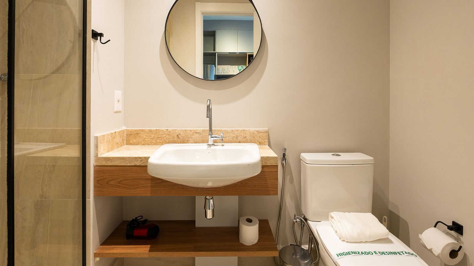 A bathroom with a round mirror, a sink, a toilet, and a shower.