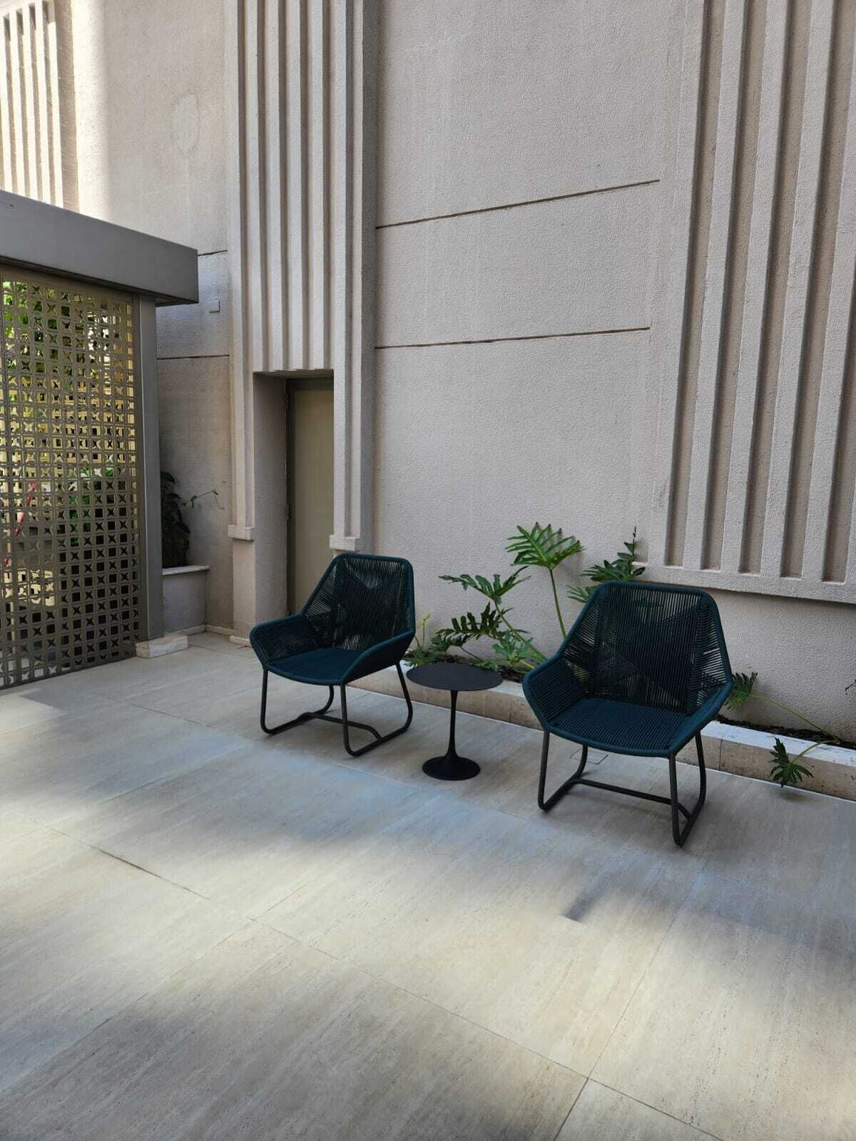 A modern outdoor seating area with two dark green chairs and a small round table, set against a textured wall with vertical lines.