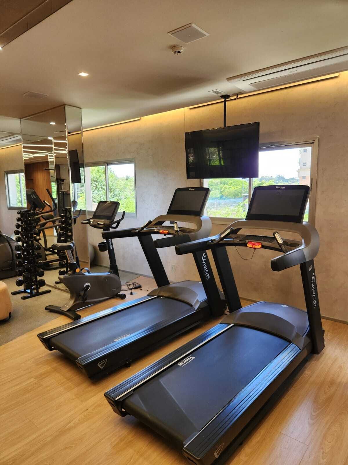 A gym with treadmills, weight machines, and a TV screen.