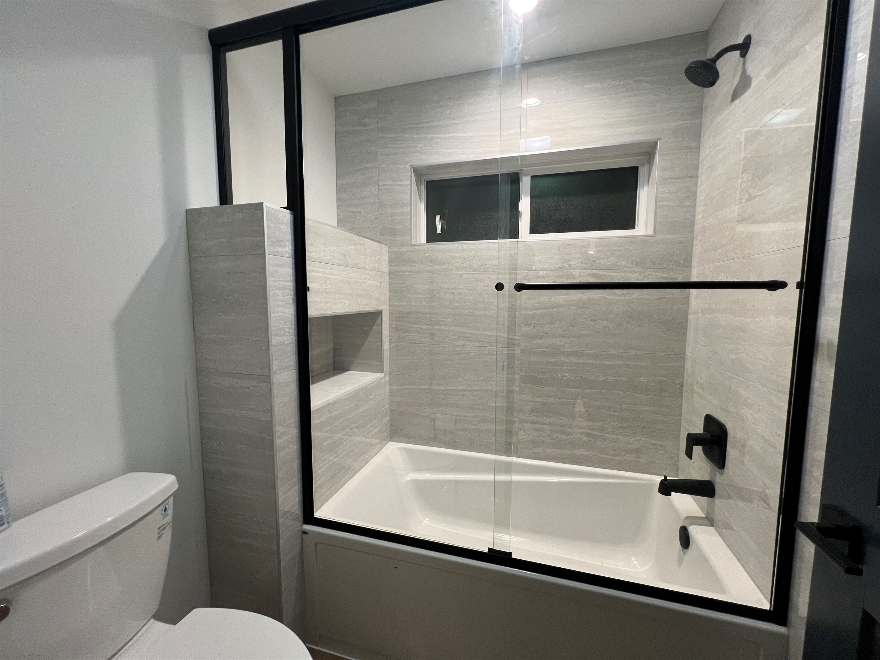 Een moderne badkamer met een douche met glazen wand, een witte badkuip en een toilet.
