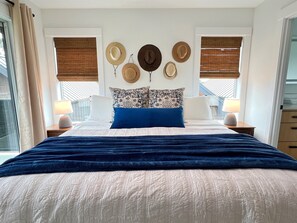 A bedroom with a large bed, two bedside tables with lamps, a wall with hats, and a window with blinds. - 2 Villas • Sleeps 21 • Theater • Sauna • Hot Tubs (Ocean Shores)