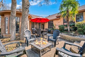 An outdoor patio with Adirondack chairs, a fire pit, and a red umbrella. - Spacious Gem, Hot Tub, 10 Min to AT&T & DFW | JCE (Grand Prairie)
