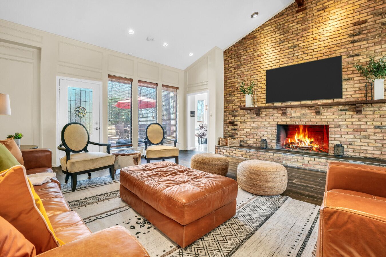 A spacious living room with a brick fireplace, leather sofas, and a large flat-screen TV mounted on the wall.