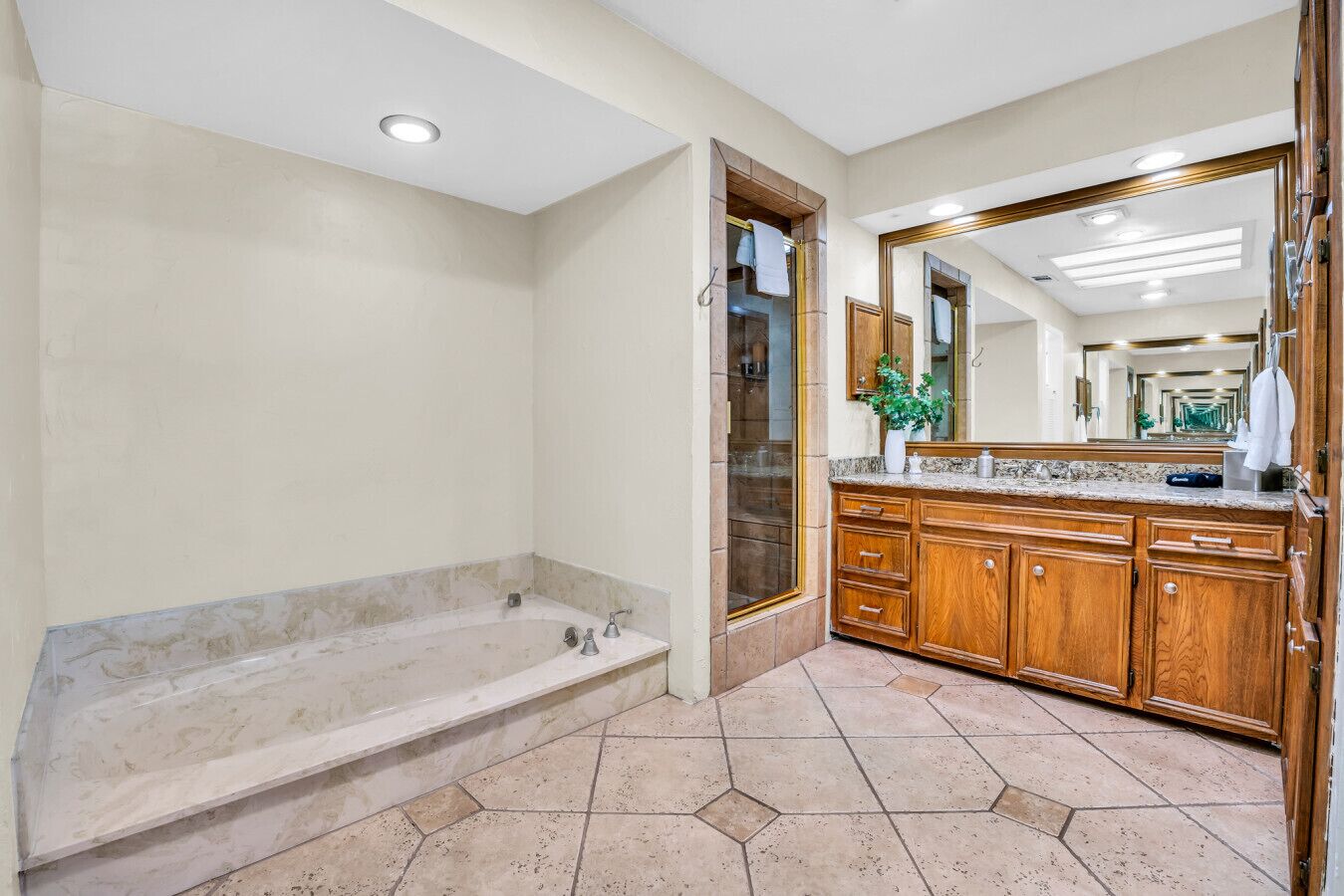 A bathroom with a large bathtub, wooden vanity, and a large mirror.
