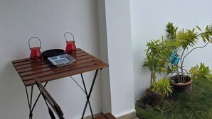 Een klein terras met een houten tafel en stoel, een plant in pot en een wanddecoratie.