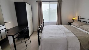 Een slaapkamer met een bed, een bureau, een stoel, een kledingkast en een raam met gordijnen.